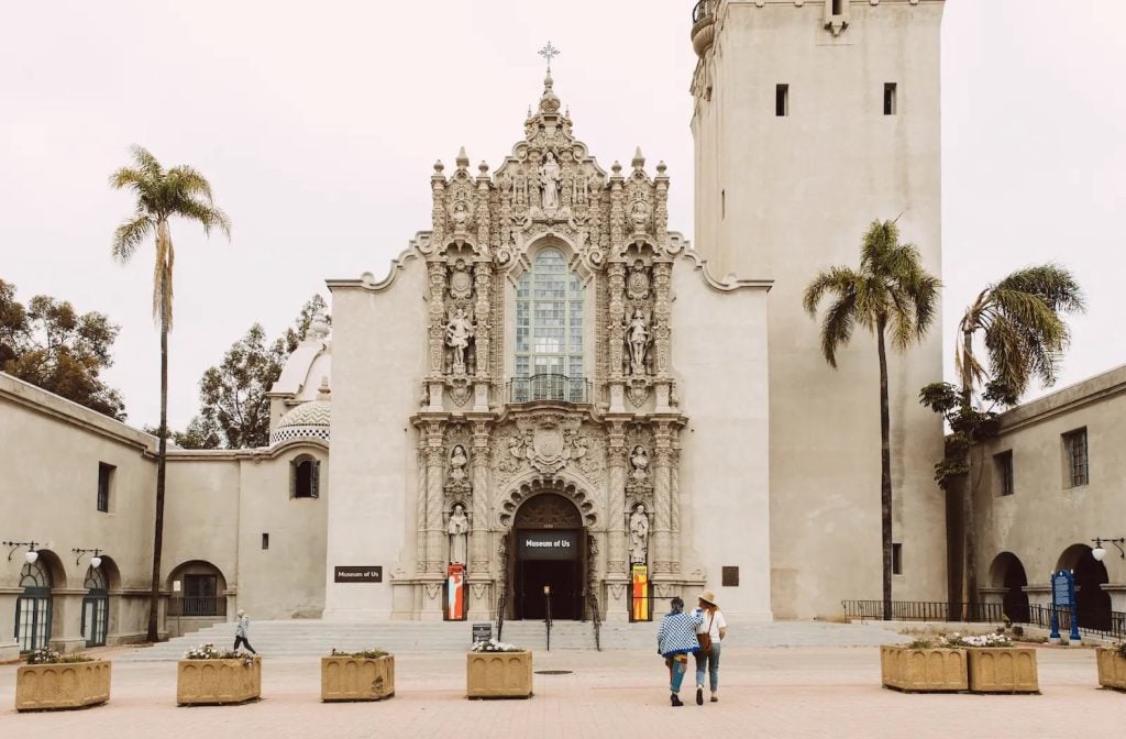 Exterior of the San Diego Museum of Us featuring two people standing out front at the Prado tower in Balboa Park, San Diego